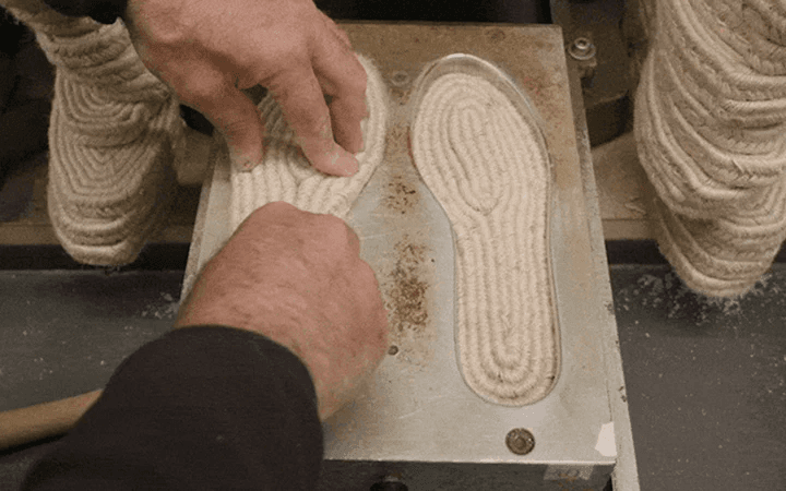 Hands arranging a coiled rope sole on a work surface.