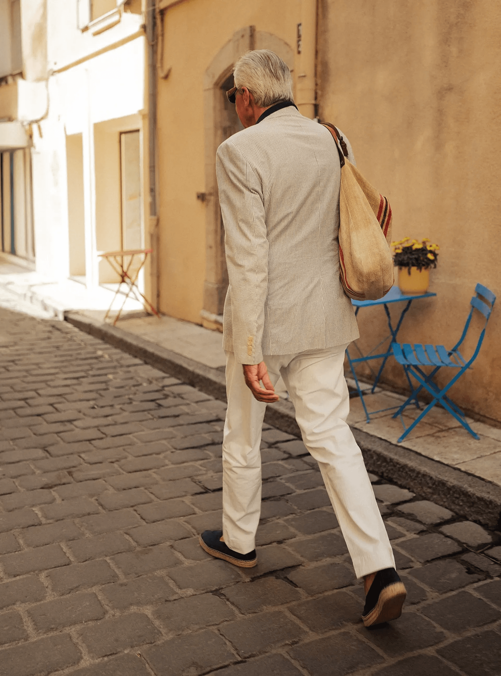 A man in a light suit walking along a sunlit street.
