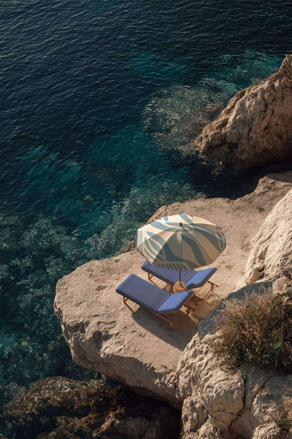 A striped parasol and deckchairs on a rocky edge above the sea.